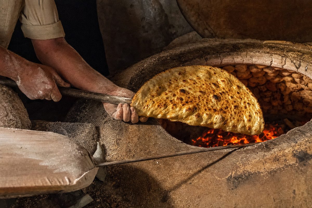 پخت نان سنگک تازه در تنور سنگی سفره‌خانه